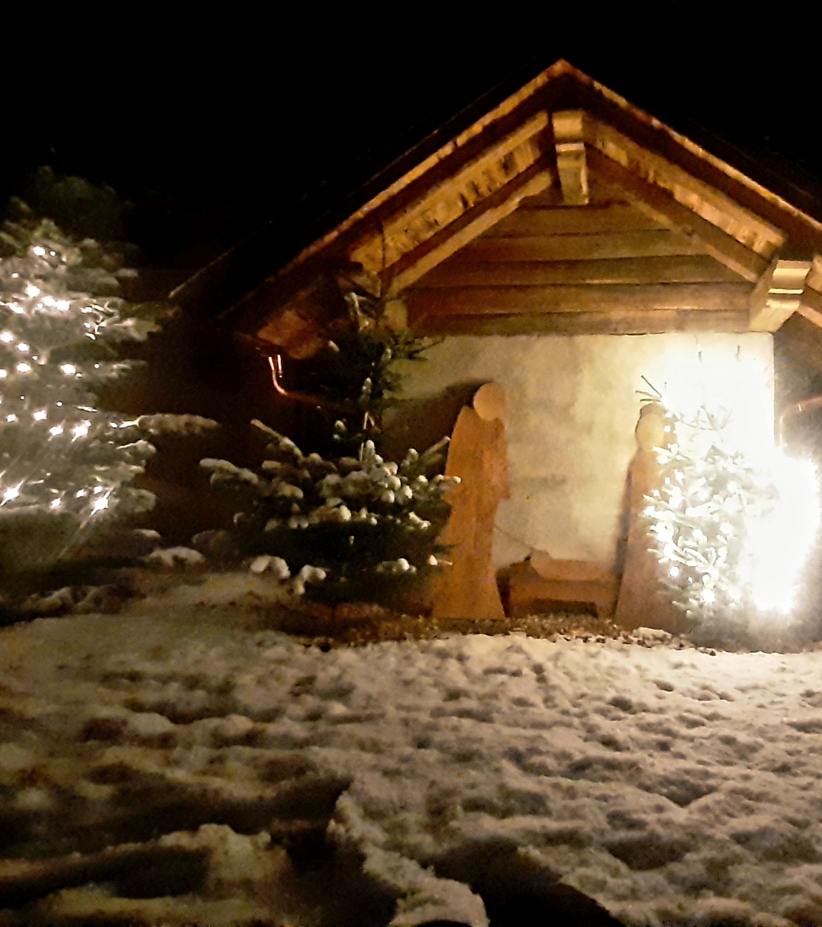 Winterbackofen mit Krippe im Dunkeln Schneebedeckter Garten, im Hintergrund ein Backofen mit Krippenfiguren